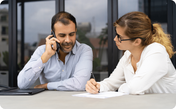 Seated outdoors near a Kailua counseling office, a focused man makes a phone call while an attentive woman takes notes during a complimentary 15-minute consultation to discuss therapy possibilities.